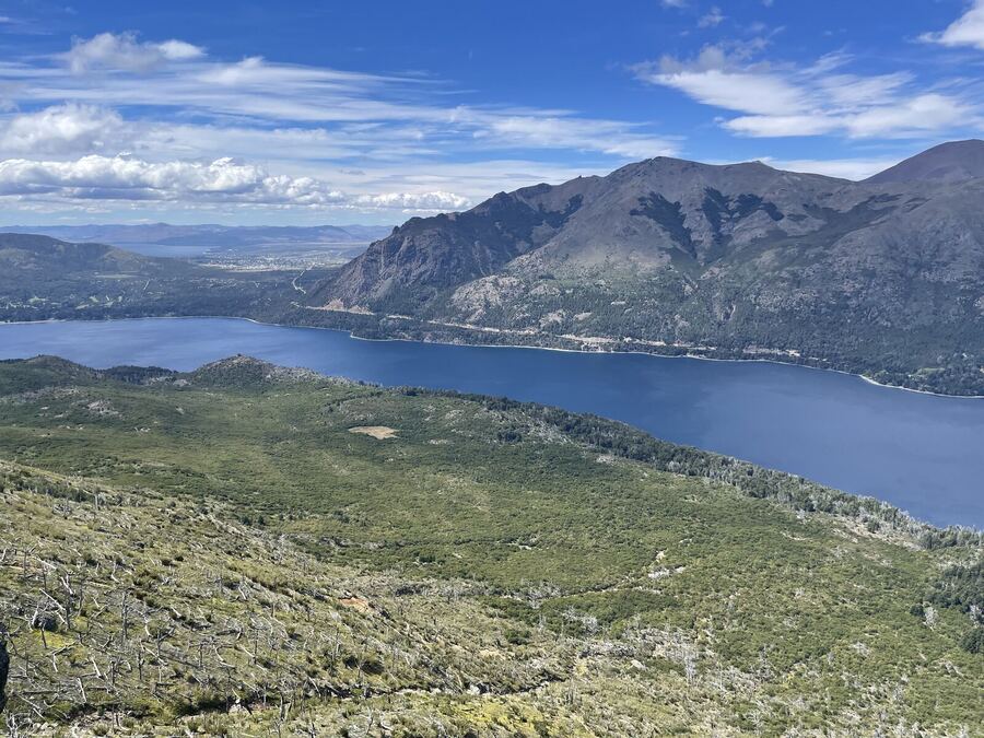 A deep blue lake winding between green hills below a massive peak