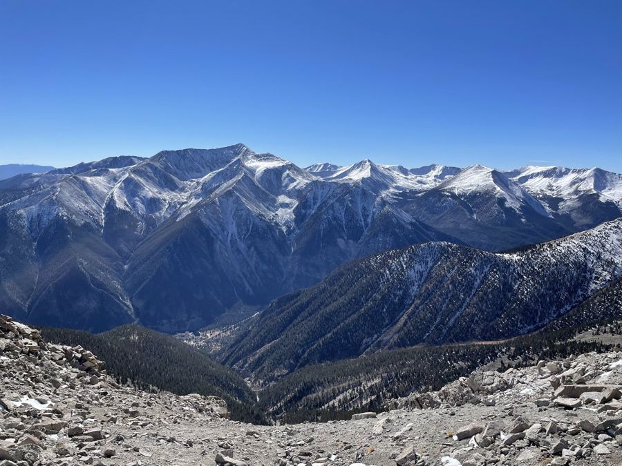 A range dusted with early snow under a deep blue sky, seen from a rocky summit