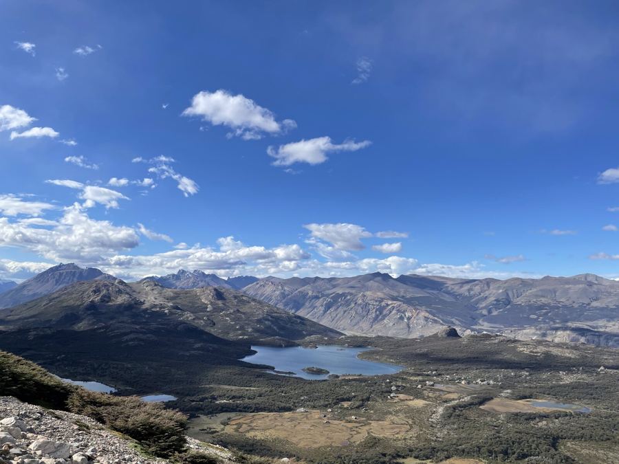 Blue lakes in a wide valley under scattered clouds, mountains folding away behind