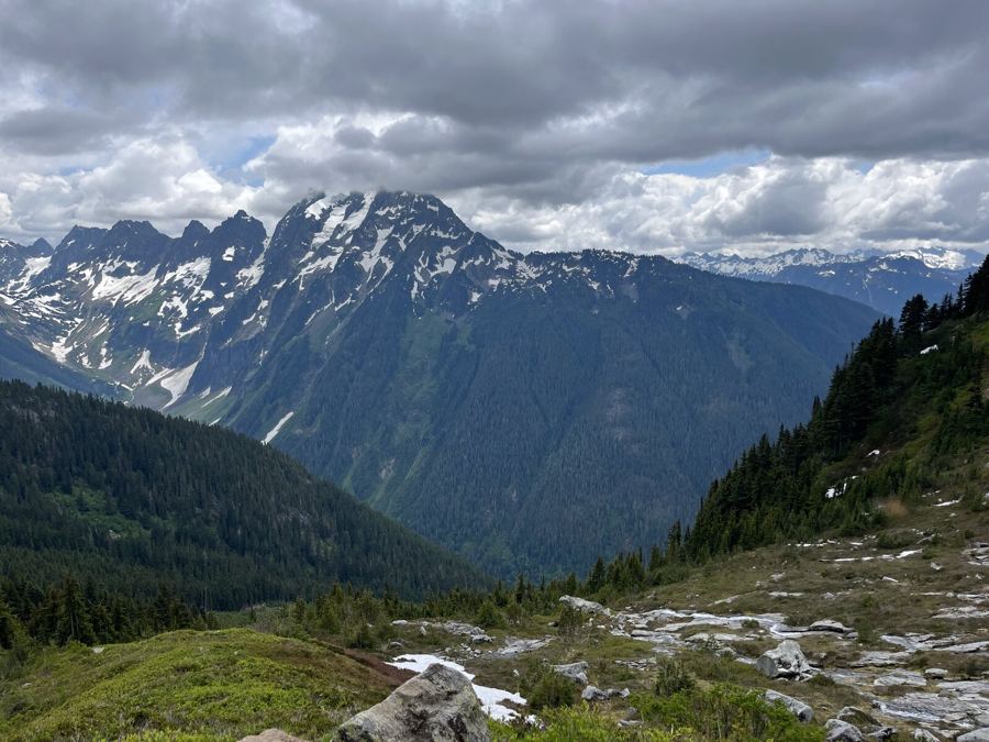 Jagged snowy peaks across a deep forested valley under heavy cloud